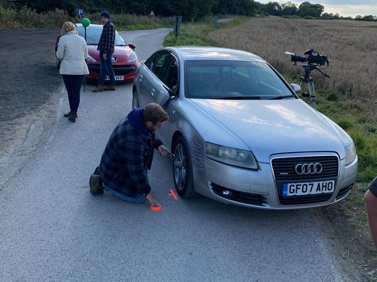 Silver Audi A6 beside a rural road during filming preparation